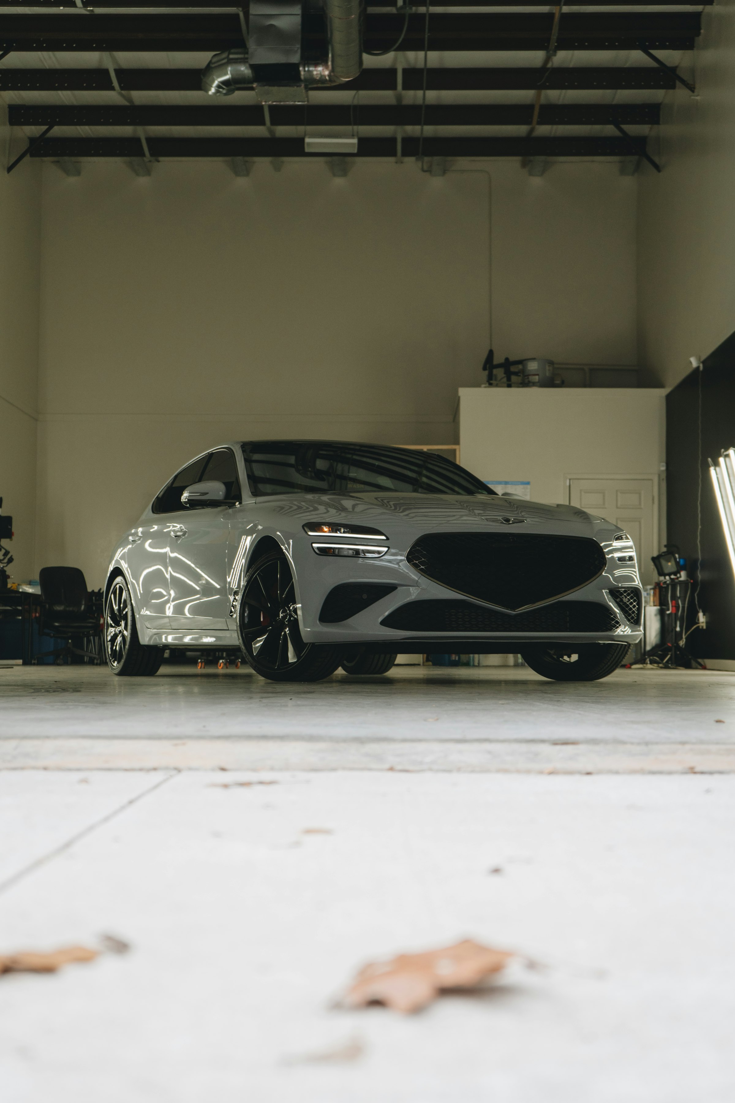 Sports sedan front-three-quarter, low-angle in a clean shop bay with exposed-beam ceiling